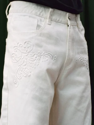 Close-up of tonal scroll embroidery and front pocket detail on white wide leg denim jeans