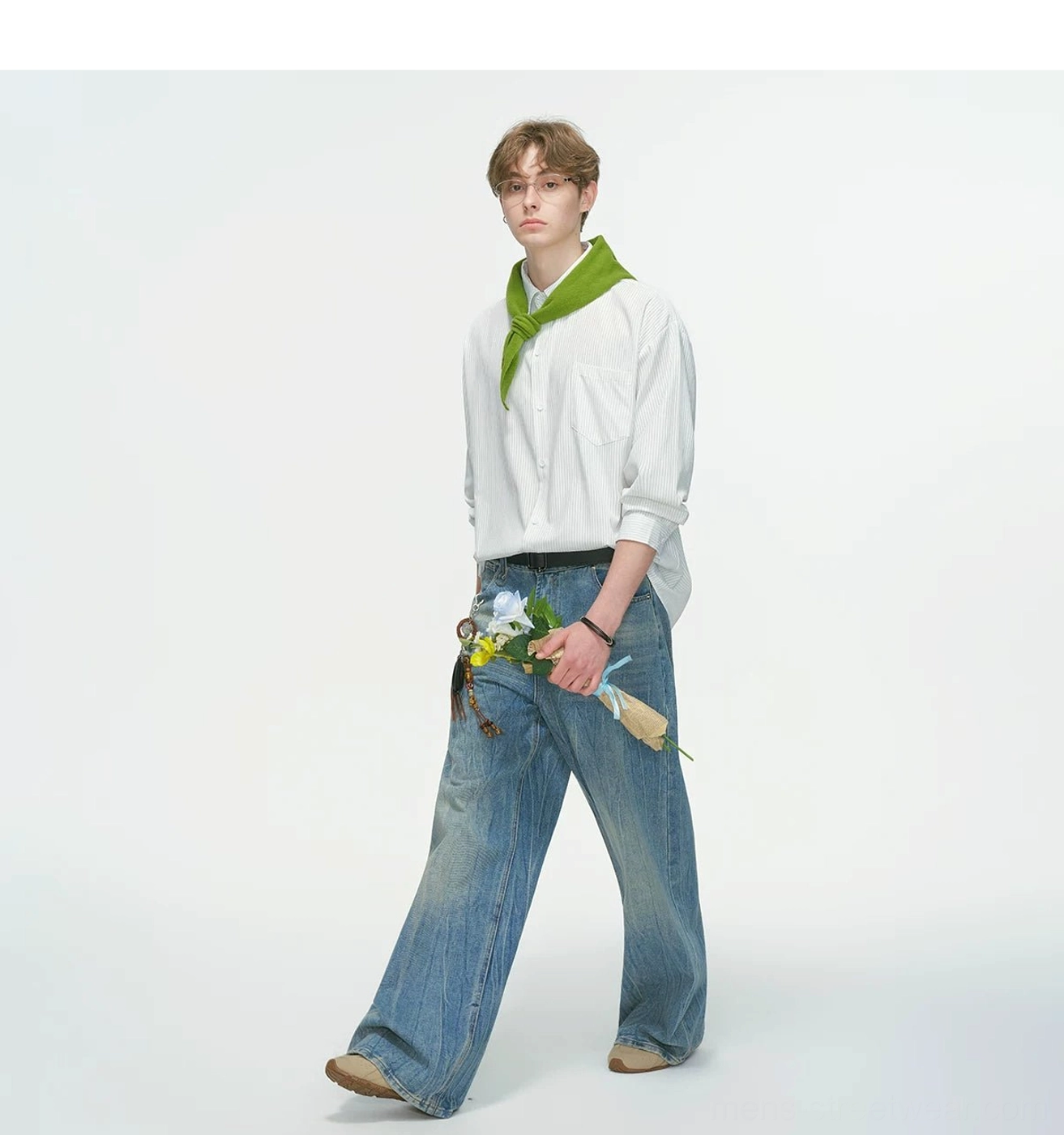 Male model walking in a white vertical stripe relaxed overshirt with wide-leg blue jeans, green neck scarf, flower bunch, and casual loafers