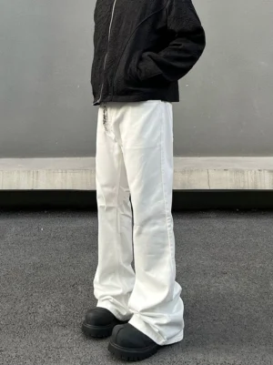 Low-angle front-side view of white wide flare jeans styled with a black cropped zip jacket, waist chain, and black platform shoes in a Korean streetwear outfit