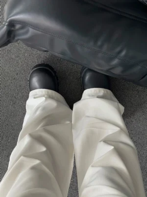White wide leg pleated trousers with crisp front folds styled over thick-soled black leather shoes with a black bag