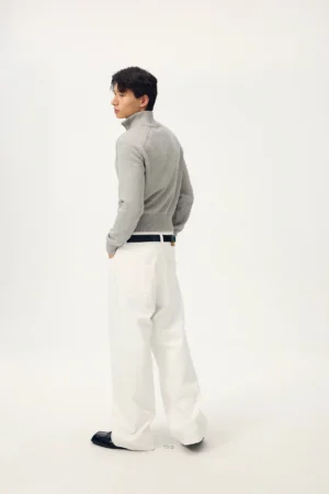 Side-back view of a male model wearing white wide-leg streetwear trousers with a fitted grey knit top in a clean studio setting