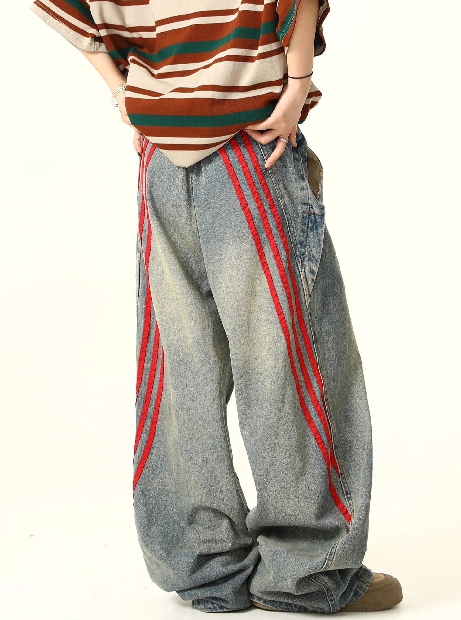 Back three-quarter view of wide-leg blue denim jeans featuring full-length red triple-stripe accents along both outer legs and a faded vintage wash