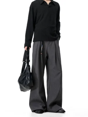 Dark gray wide-leg tailored trousers with soft drape styled with a black ribbed polo shirt and leather tote bag