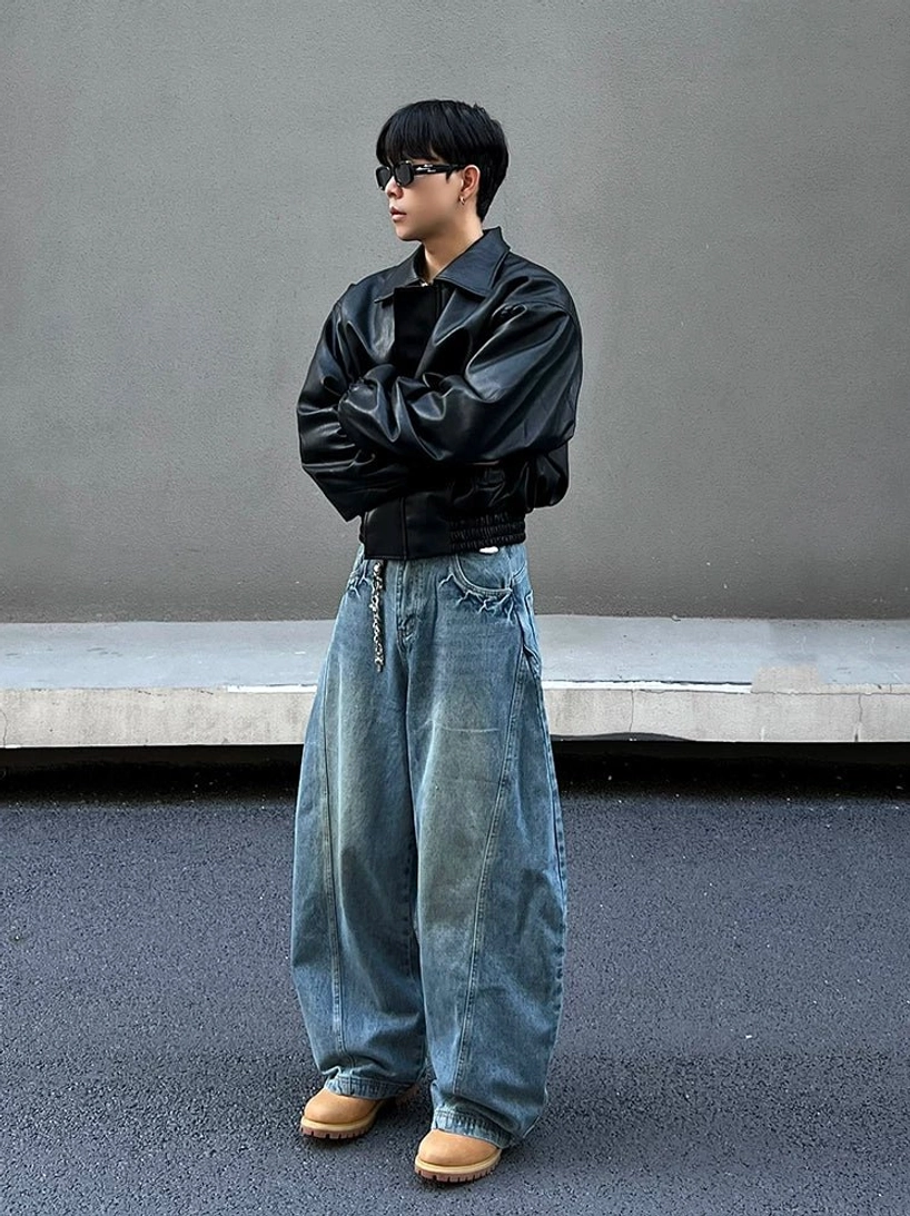 Side full-body view of wide-leg orbital panel jeans showing the rounded balloon shape, curved side seam, vintage blue wash, tapered hem, and stacked streetwear fit