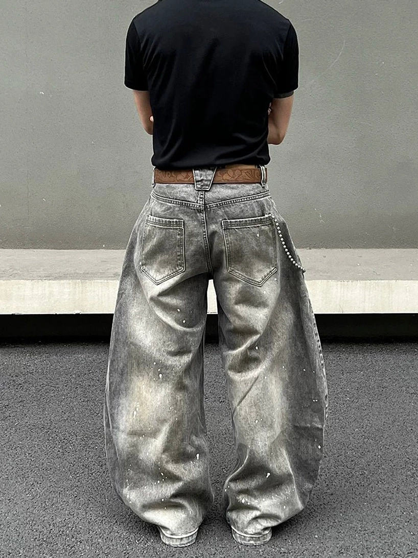 Rear view of wide-leg paint-splatter denim jeans showing classic back patch pockets, faded ash gray wash, loose balloon silhouette, and stacked streetwear drape