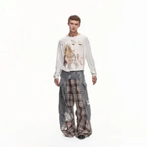 Full front view of a model wearing wide-leg plaid cargo pants with a detachable waist panel, washed grey utility overlays, graphic embroidery, long-sleeve streetwear top, and black leather shoes
