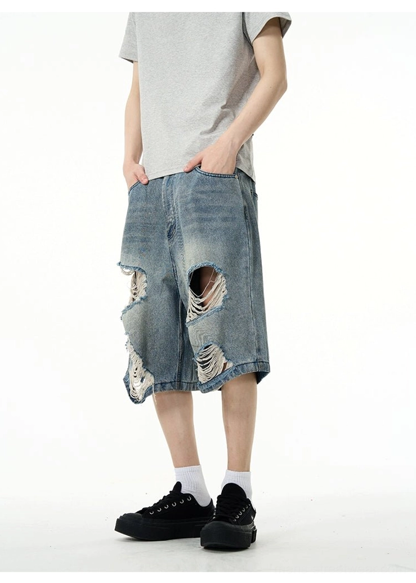 Side view of wide-leg ripped denim Bermuda shorts showing the relaxed oversized silhouette, knee-length cut, socks, and black loafers