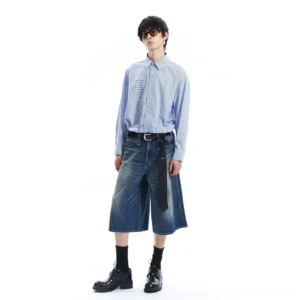 Full body front view of wide leg washed blue denim Bermuda shorts styled with a light blue shirt black socks and derby shoes