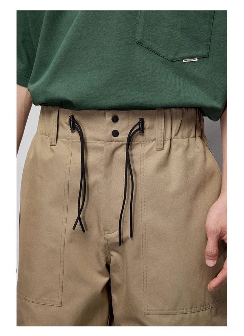 Close-up of khaki relaxed streetwear pants showing dual black drawstrings, button waistband, patch pockets, and cotton-blend fabric