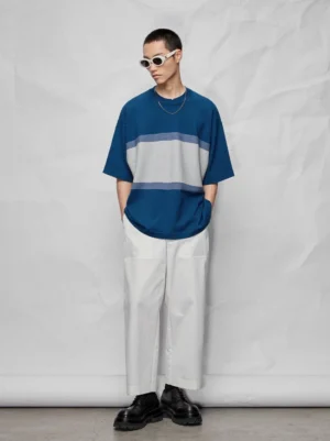 Front view of wide white cropped streetwear pants styled with a color-block striped oversized tee and white frame sunglasses