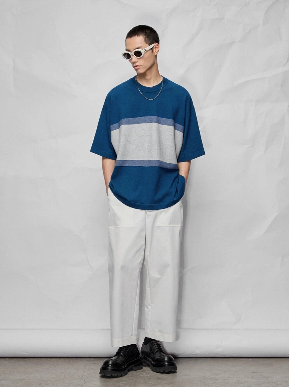 Front view of wide white cropped streetwear pants styled with a color-block striped oversized tee and white frame sunglasses