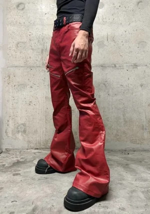 Male model wearing wine red coated flare jeans with fitted high waist, silver zipper hardware, stacked flared legs, black top, studded belt, and platform boots