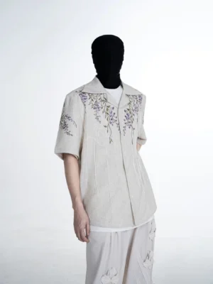 Three-quarter view of a relaxed linen-look camp shirt with cascading purple wisteria embroidery on the collar, shoulders, and chest