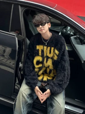 Yellow fuzzy graffiti letter oversized crewneck streetwear sweater worn by male model beside a red car