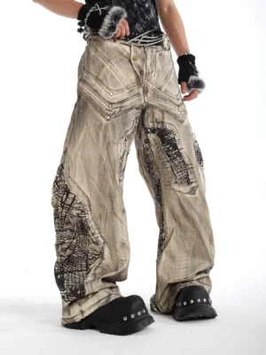 Yellow mud fossil vein wide-leg distressed streetwear jeans shown from a low front side view with black graphic patch panels and studded pocket details
