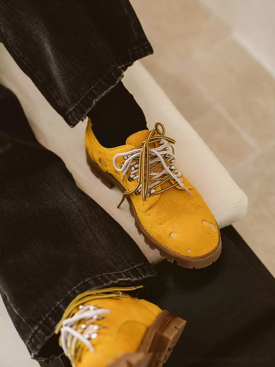 Model wearing mustard yellow spotted pony-hair derby shoes with black jeans and black socks in a modern streetwear outfit