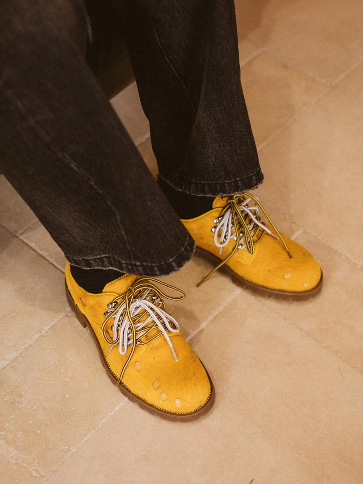 Front angled view of mustard yellow spotted pony-hair leather derby shoes showing rounded toe, metal lace hardware, and rugged outsole